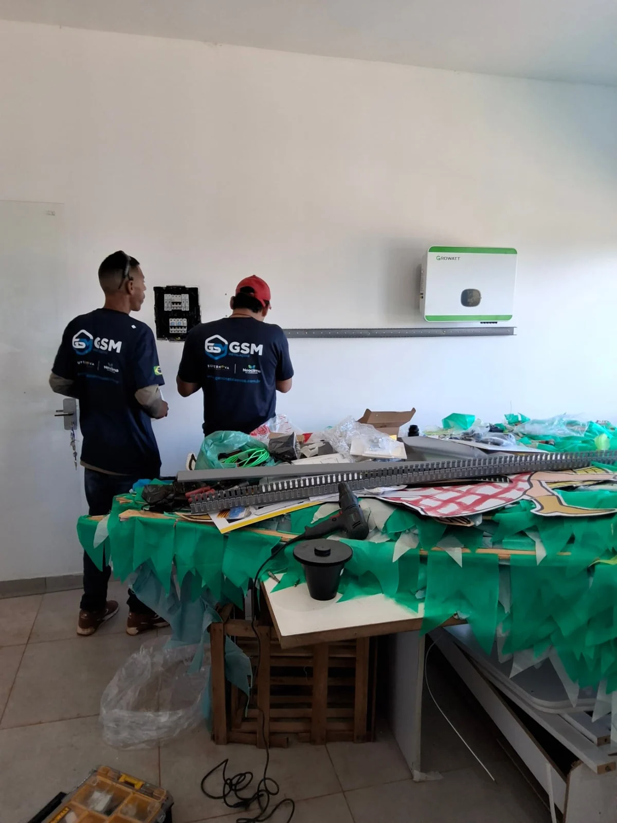 Equipe trabalhando junto a quadro de proteção e inversor fotovoltaico fixados na parede
